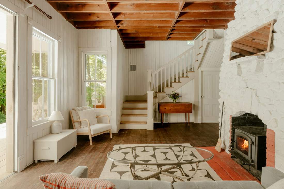 Bright cottage living space with a wood ceiling, fireplace and patterned rug